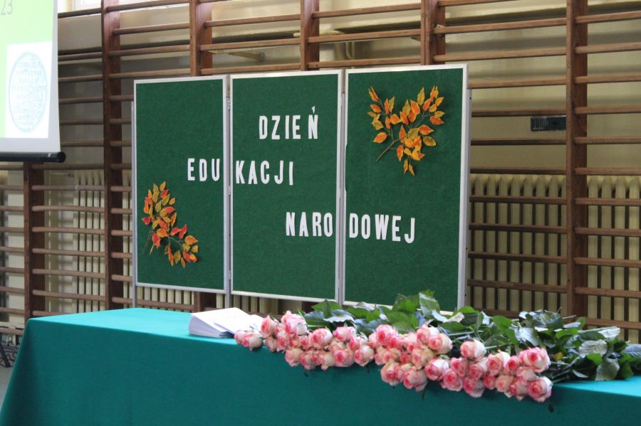 tablica z napisem dzień edukacji narodowej, przed tablicą stół z kwiatami